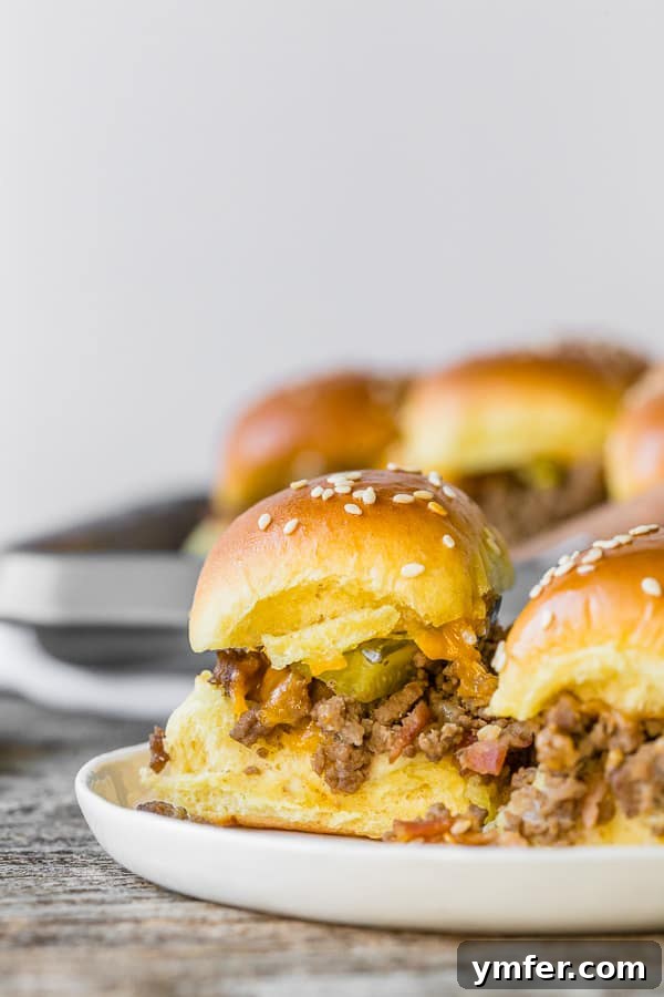 Cheesy Bacon Pull-Apart Sliders 3 A close-up view of two baked bacon cheeseburger sliders, showing the melted cheese, bacon, and pickles spilling out.
