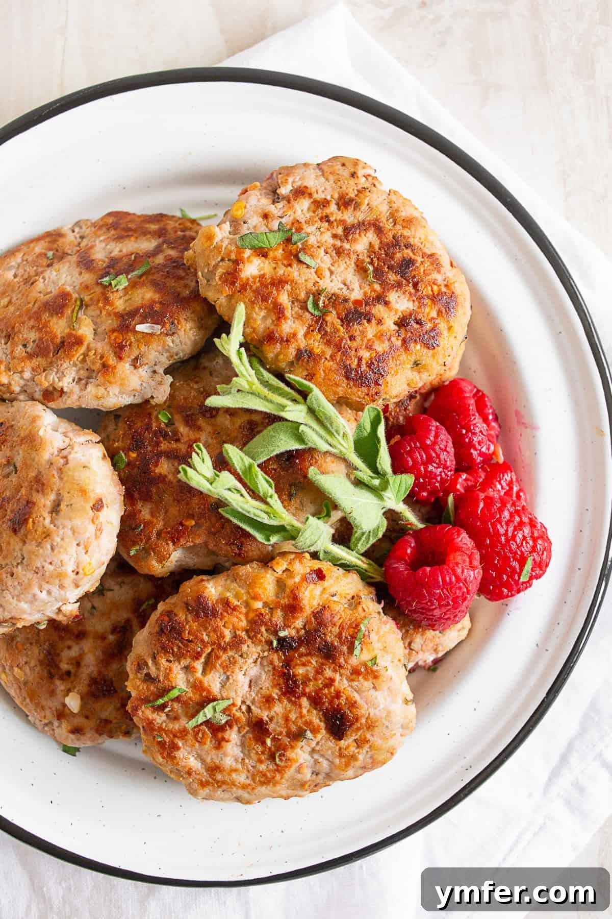 Handcrafted Chicken Sausage Patties 2 Chicken sausage patties on a plate with fresh berries and herbs.