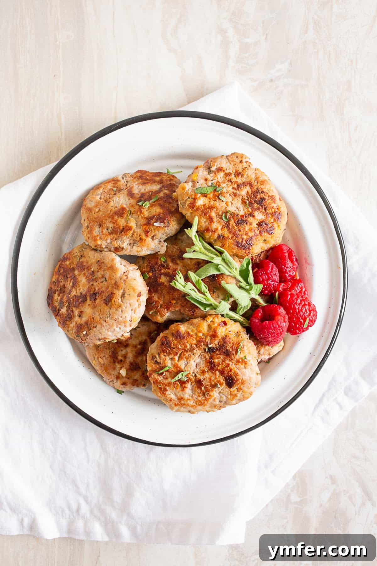 Handcrafted Chicken Sausage Patties 4 Homemade Chicken Sausage Patties on a plate with fresh herbs and berries.