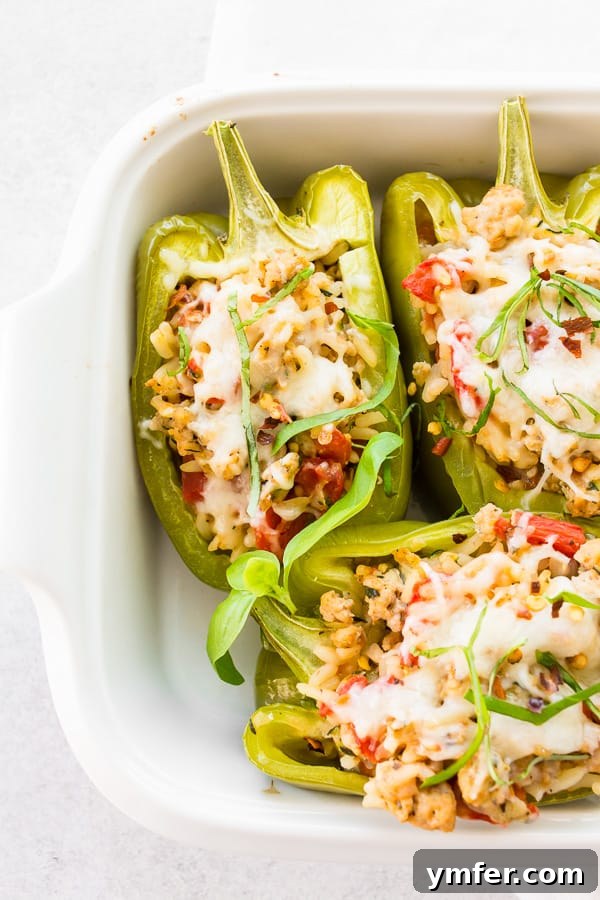 Savory Chicken Stuffed Bell Peppers 2 Ground Chicken Stuffed Bell Peppers in a small white casserole pan, beautifully golden brown and ready to serve