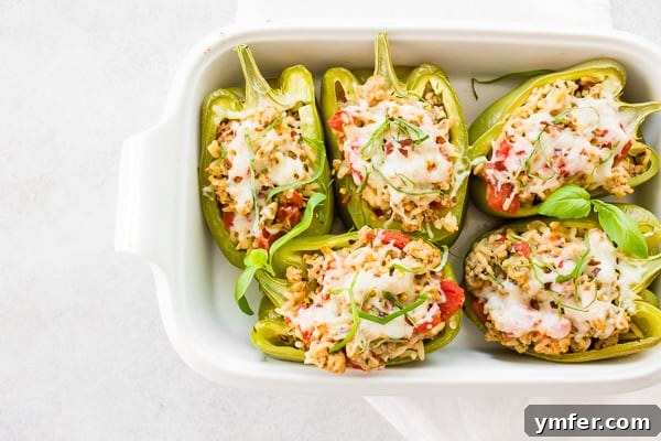 Savory Chicken Stuffed Bell Peppers 4 Three golden-brown Ground Chicken Stuffed Bell Peppers nestled in a white baking dish, fresh from the oven