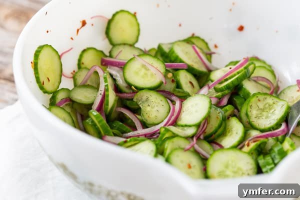 Crisp and Cool Cucumber Salad 3 Close-up shot of a white bowl filled with glistening, thinly sliced cucumber and red onion salad.