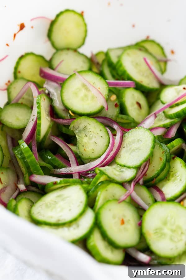 Crisp and Cool Cucumber Salad 5 Close-up detail of thinly sliced cucumbers glistening with dressing in a white bowl.