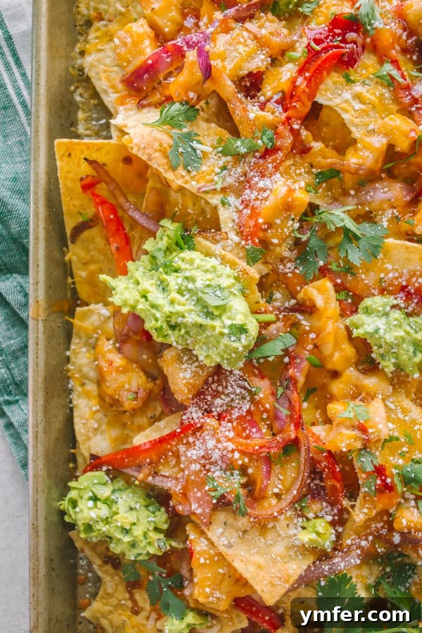 Sweet Heat Thai Chicken Nachos 5 Close up of loaded Thai sweet chili chicken nachos on a sheet pan, showing chicken, cheese, onions, guacamole and cilantro.