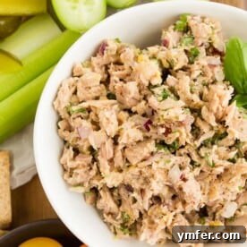 lemon herb tuna salad in a white bowl surrounded by cracker and vegetables