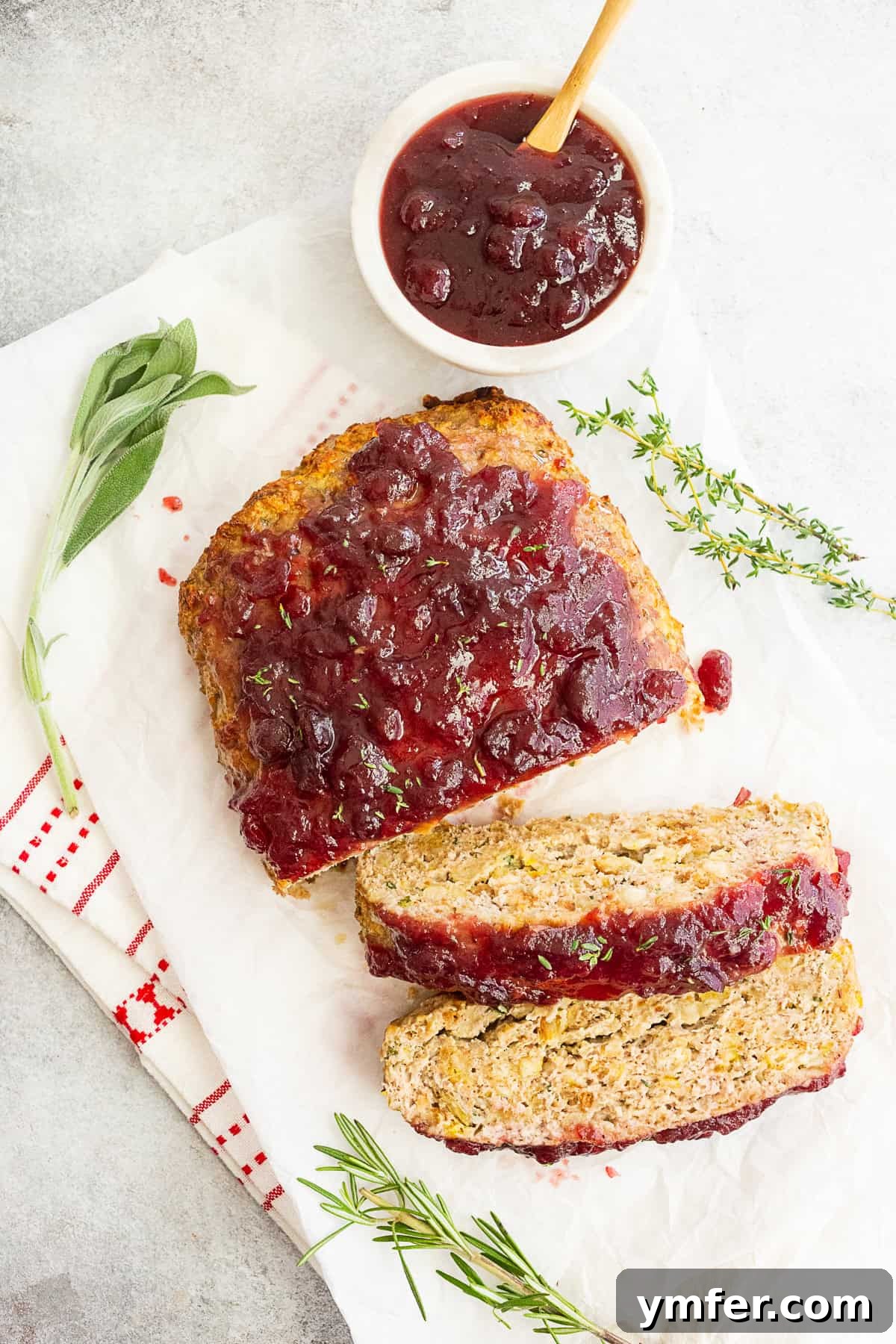 Festive Turkey Meatloaf 2 Thanksgiving turkey meatloaf sliced and staged with fresh herbs and extra cranberry sauce, ready to be served.