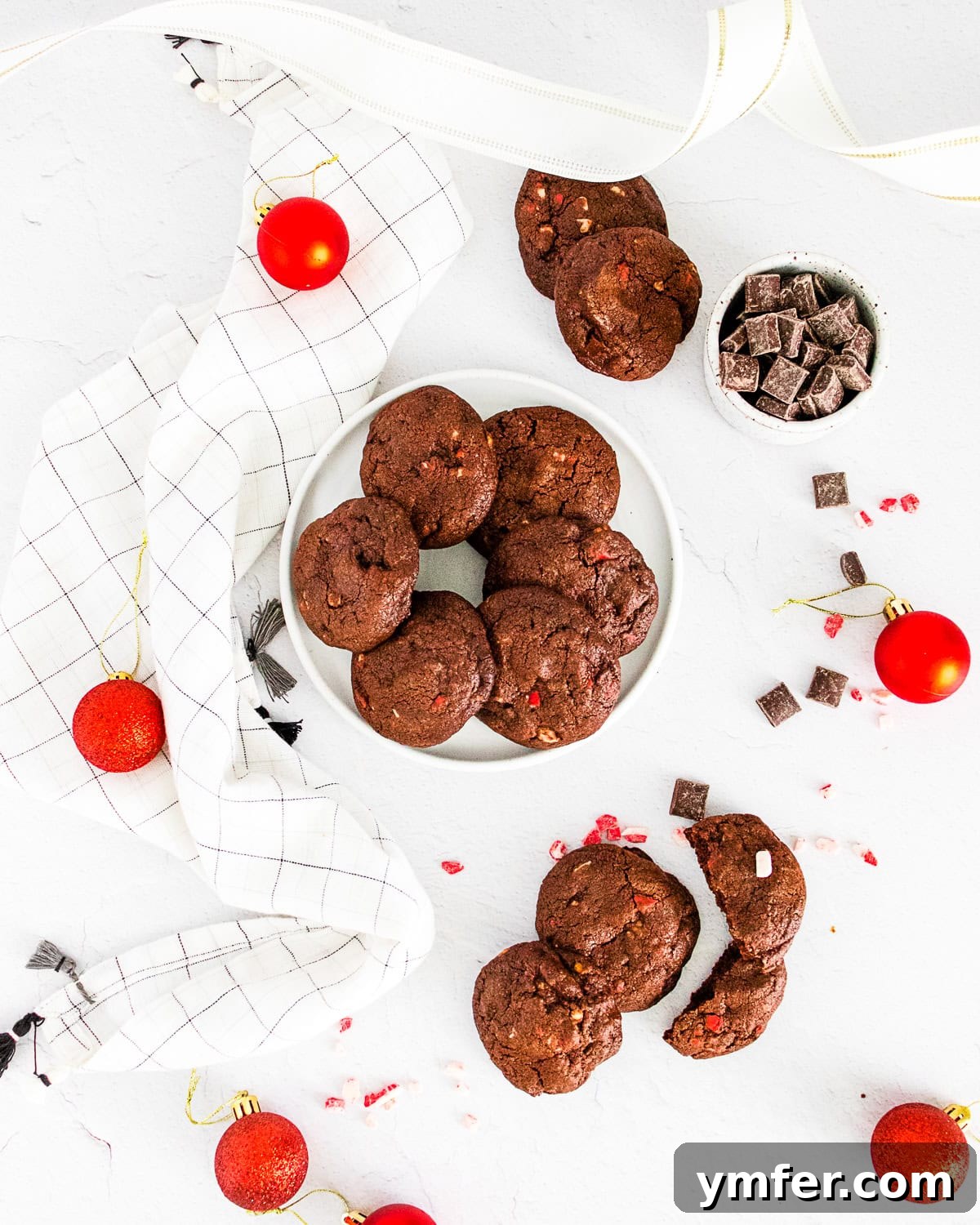 Peppermint Chocolate Bark Bites 2 Indulgent chocolate peppermint bark cookies on a pristine white table, surrounded by scattered chocolate chips, ready for holiday festivities.
