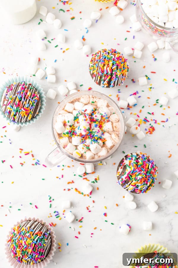 Sprinkle Surprise Strawberry Chocolate Hot Cocoa Bombs 3 Two chocolate strawberry funfetti hot chocolate bombs sit elegantly on a white table, one next to a steaming mug of prepared hot chocolate, showcasing their delightful appearance.