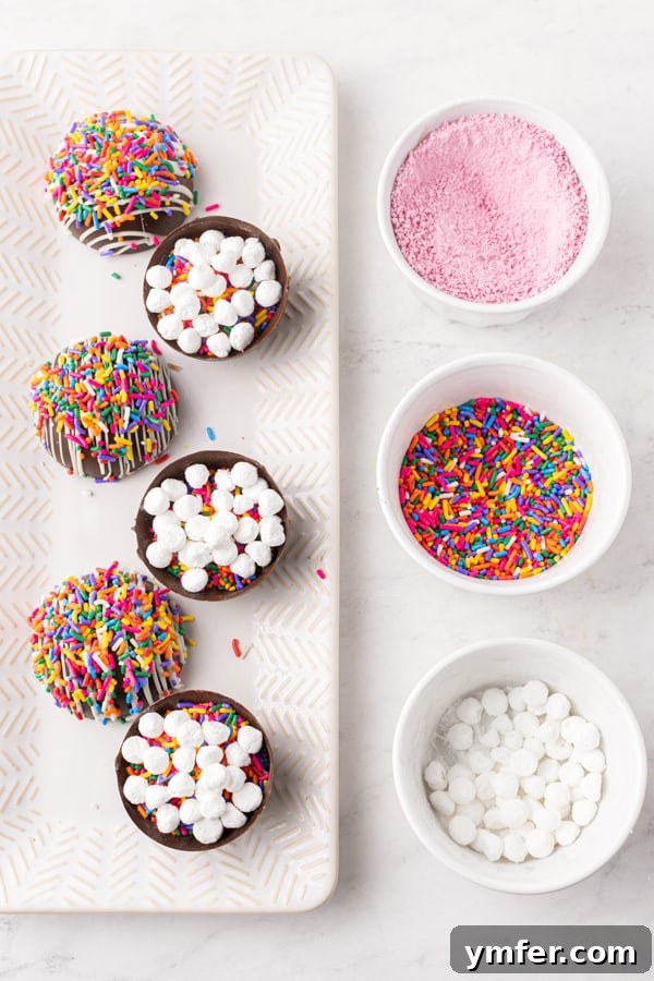 Sprinkle Surprise Strawberry Chocolate Hot Cocoa Bombs 4 A baking sheet showcasing several half-made chocolate strawberry funfetti hot chocolate bombs, some coated in chocolate, others filled, demonstrating the assembly process.