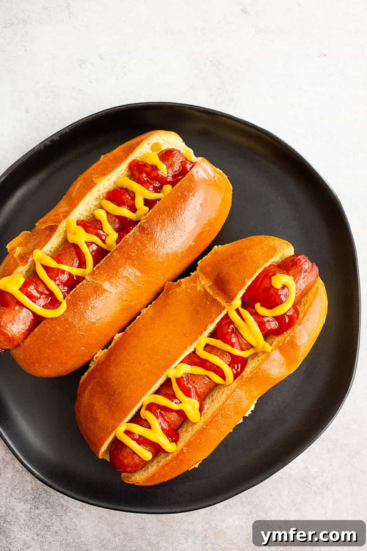 Two air fryer cooked hot dogs sitting on a plate with mustard and ketchup.