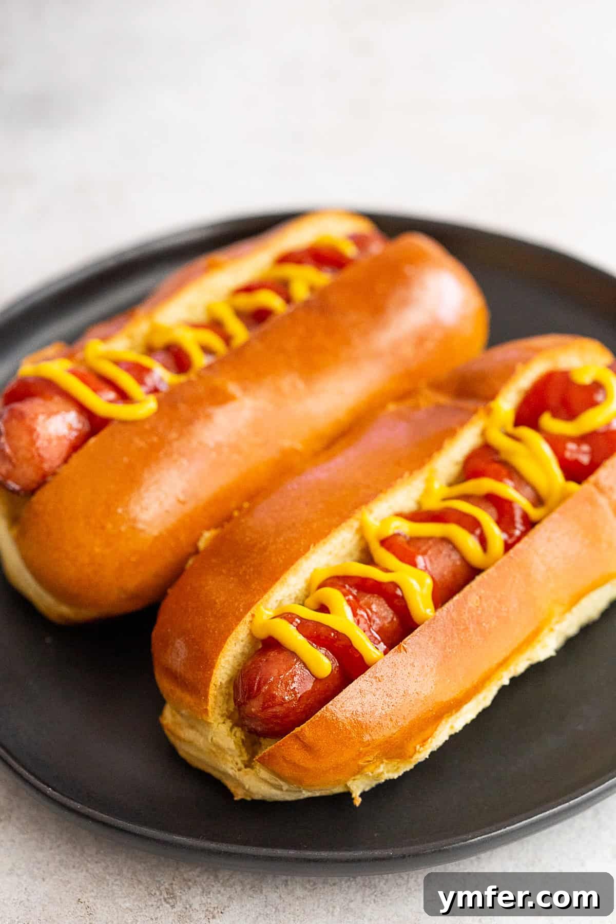 Air fryer hot dogs on a plate with yellow mustard and ketchup.
