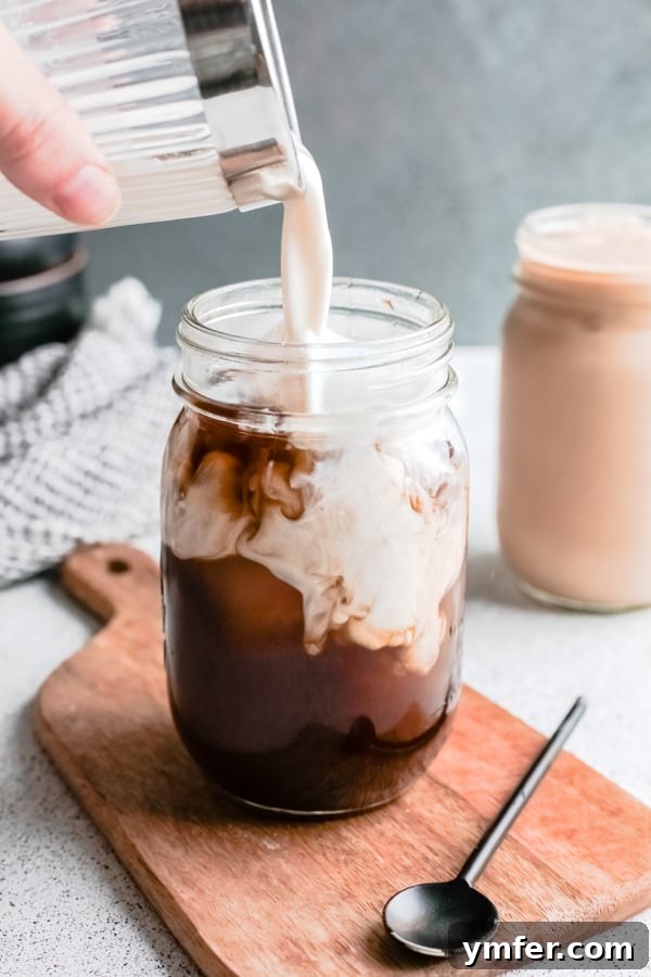 Golden Brown Sugar Shaken Espresso 4 Oat milk being poured into a shaken espresso glass filled with ice and frothy coffee.