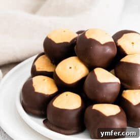 Ultimate Peanut Butter Buckeyes 11 Close-up of a plate of peanut butter buckeyes, with one featuring a perfect chocolate coating and peanut butter center.