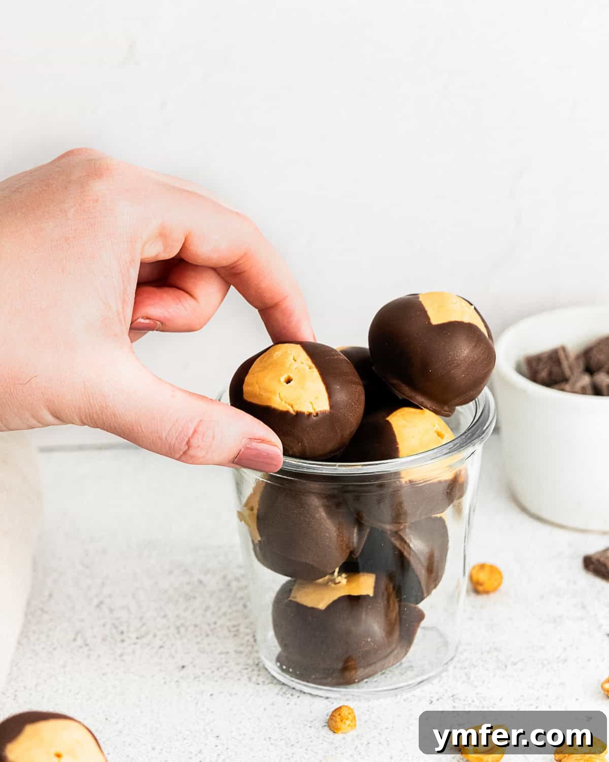 Ultimate Peanut Butter Buckeyes 3 A hand reaching for a peanut butter buckeye from a glass jar filled with candies
