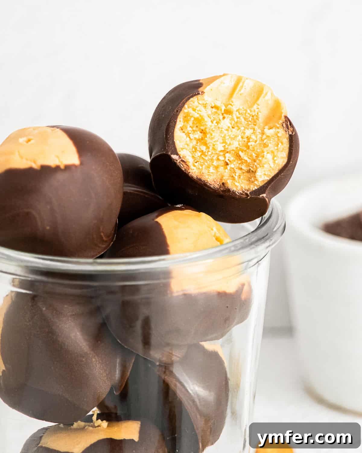 Ultimate Peanut Butter Buckeyes 6 Several peanut butter buckeyes on a plate, one with a bite taken out, showing the creamy peanut butter inside