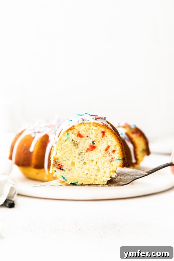Red, White, and Bundt 5 A festive Fourth of July Bundt Cake with a slice removed, showcasing its moist texture and vibrant sprinkles.