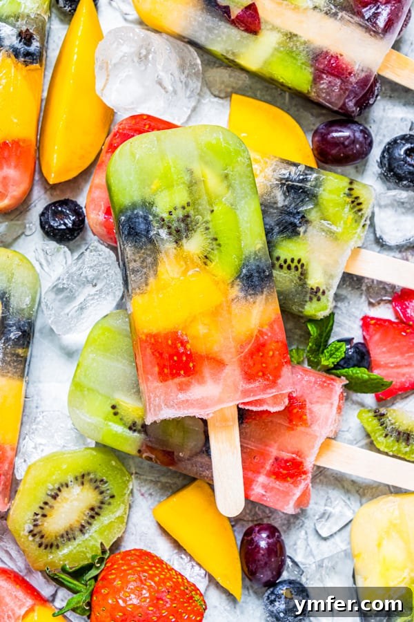A vibrant, close-up shot of a single homemade rainbow fruit popsicle, showcasing the distinct layers of red, orange, yellow, green, and blue fruits perfectly frozen.