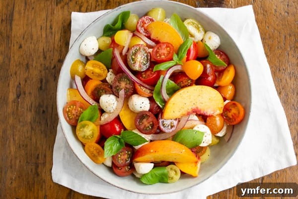 Sun-Kissed Peach Tomato Caprese 7 Tomato Peach Caprese Salad in a bowl sitting on a wood table.
