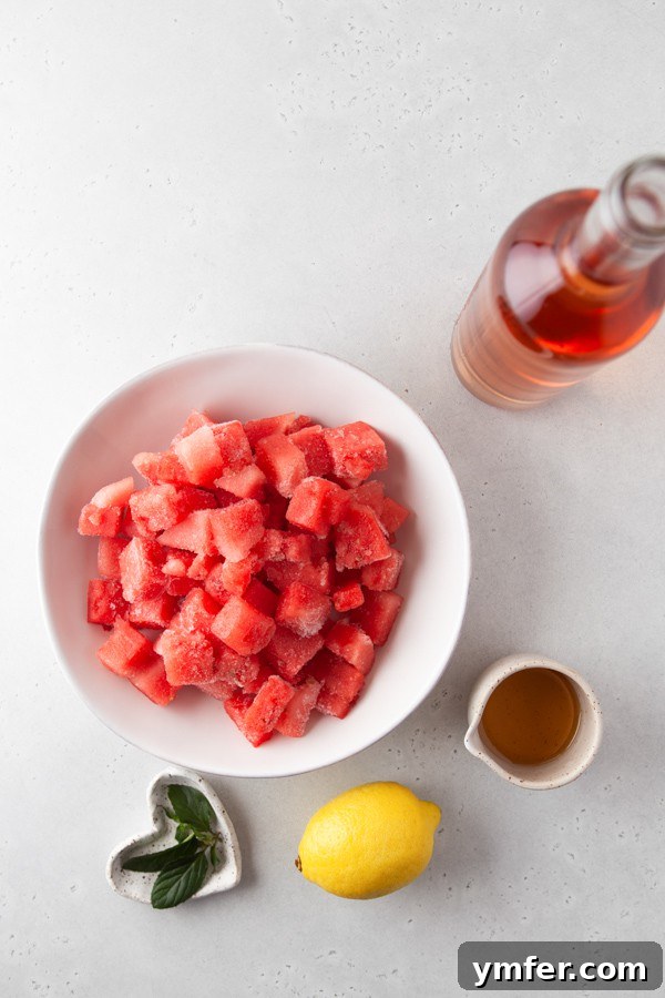 Essential ingredients for crafting a delicious Watermelon Frosé laid out: a bottle of rosé wine, fresh cubed watermelon, limes, and agave nectar.