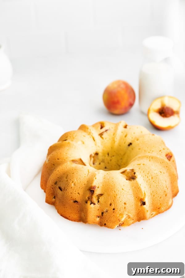 Sun-Kissed Peach Bundt 3 A beautifully baked peach bundt cake presented on a cake plate, surrounded by fresh, ripe peaches.