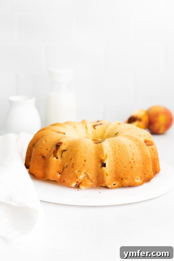 Sun-Kissed Peach Bundt 6 A full, golden-brown peach bundt cake beautifully displayed on a marble cake plate, ready to be sliced.