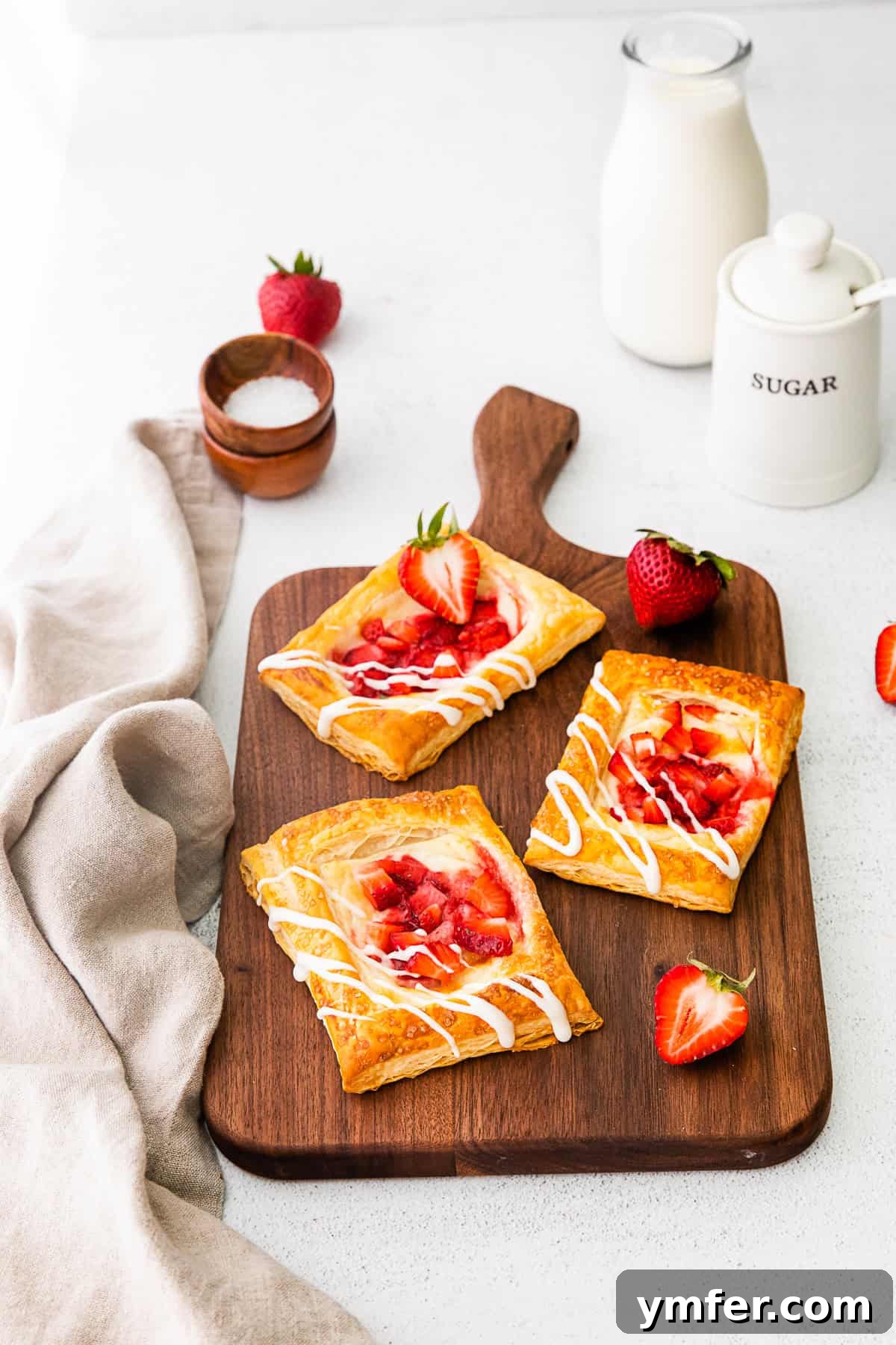 Creamy Strawberry Danish Delight 3 Easy strawberry cheesecake Danish presented on a rustic cutting board, adorned with fresh strawberries and a delicate drizzle of glaze.
