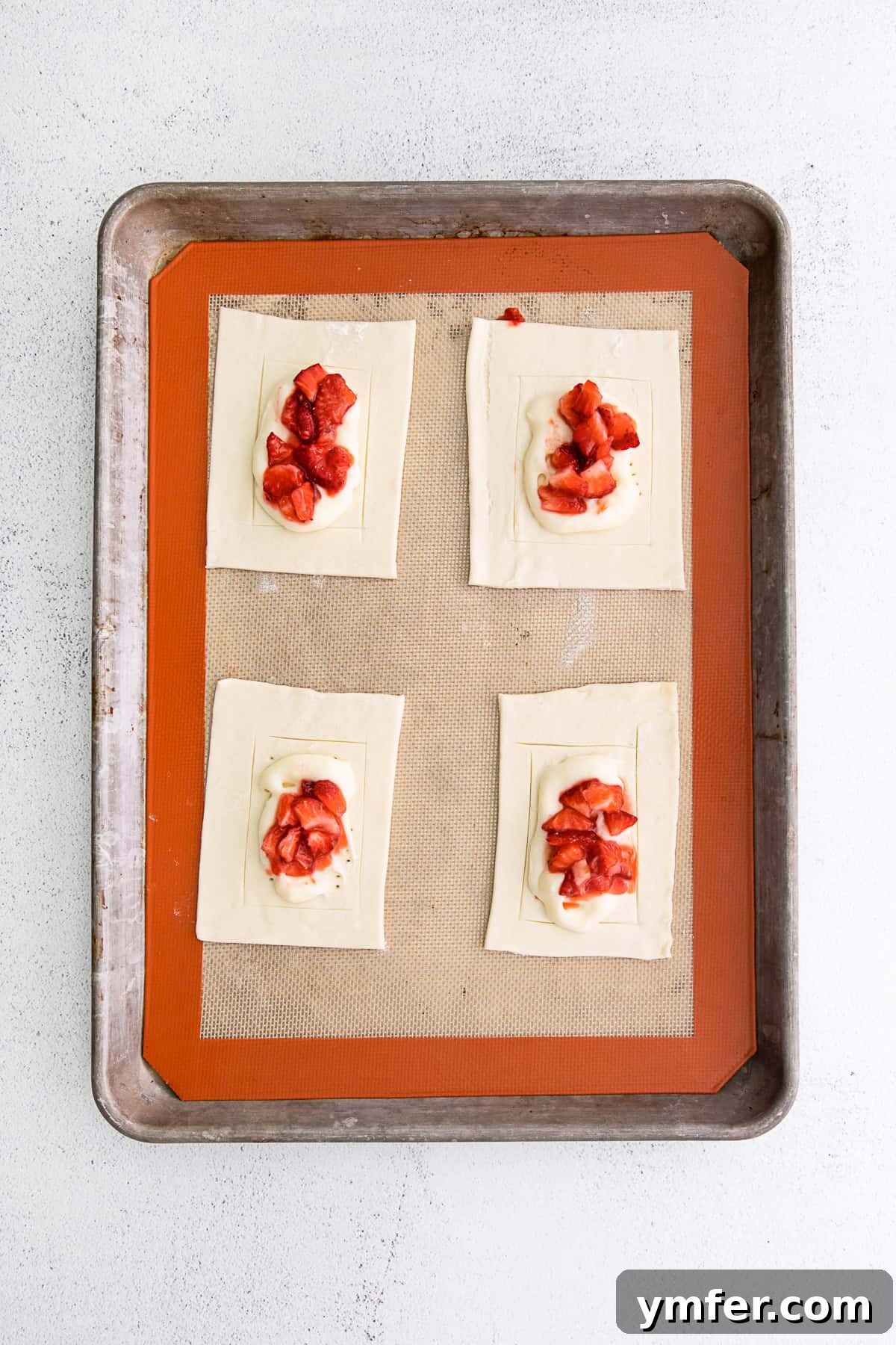 Creamy Strawberry Danish Delight 5 Individual uncooked puff pastry squares filled with cheesecake and strawberries, arranged on a baking sheet.