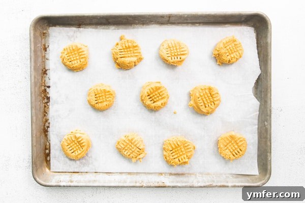 Ultimate Brown Butter Peanut Butter Cookies 4 Uncooked Brown Butter Peanut Butter Cookie dough balls arranged on a parchment-lined sheet pan, ready for baking and fork pressing.