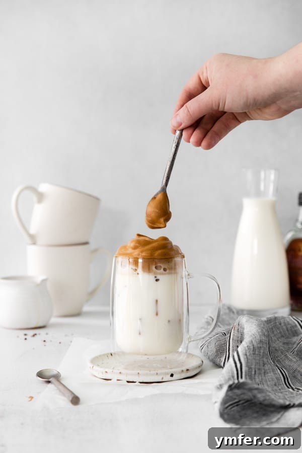Maple Velvet Coffee 4 A hand pouring the thick, maple-infused whipped coffee foam over a glass of iced milk, creating a beautiful layered drink.