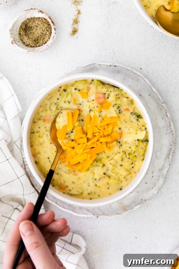 Velvety Instant Pot Broccoli Cheddar Delight 3 Close-up of a hand holding a spoon, scooping a rich portion of Instant Pot Broccoli Cheddar Soup from a white bowl, showcasing the creamy texture and generous chunks of broccoli and carrot.