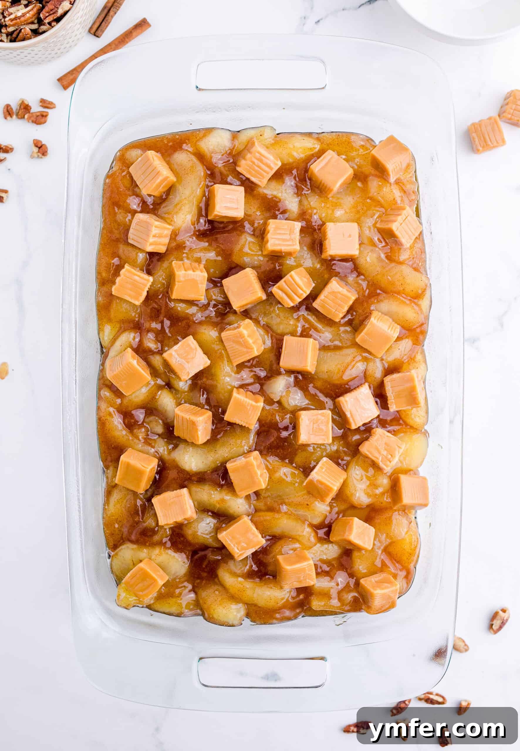 Golden Caramel Apple Bake 4 The distinct layers of uncooked Caramel Apple Dump Cake in a baking pan, showing the apple filling, caramels, and dry cake mix.