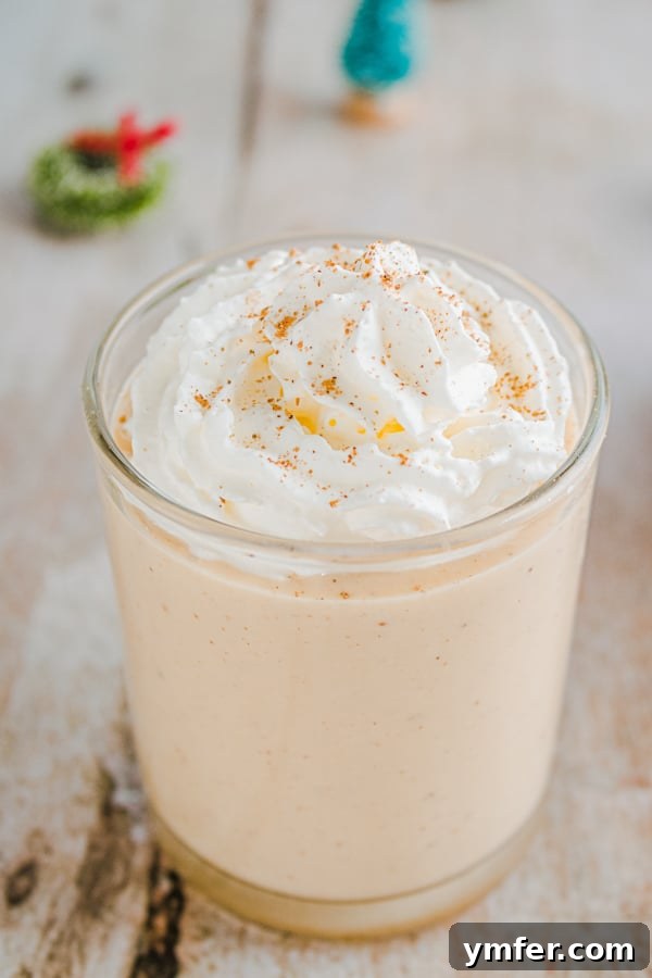 A festive glass of homemade spiced gingerbread eggnog, topped with whipped cream and a sprinkle of nutmeg.