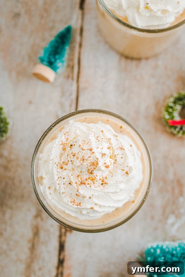Two glasses of spiced gingerbread eggnog, garnished with cinnamon sticks and star anise, sitting on a wooden surface.