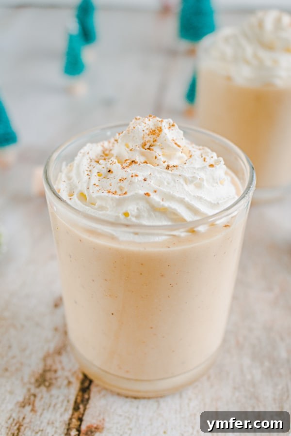 A glass of gingerbread eggnog garnished with whipped cream and a cinnamon stick, ready to be enjoyed.