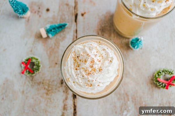 A close-up of the spiced gingerbread eggnog in a glass, with a festive bokeh background, highlighting its creamy texture.
