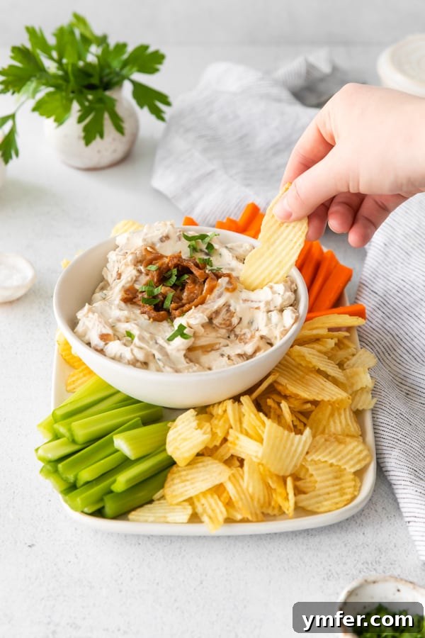 Gourmet Caramelized Onion Dip 4 A hand holding a ruffled potato chip, gracefully scooping up a generous portion of the creamy homemade French Onion Dip, highlighting its appealing texture.