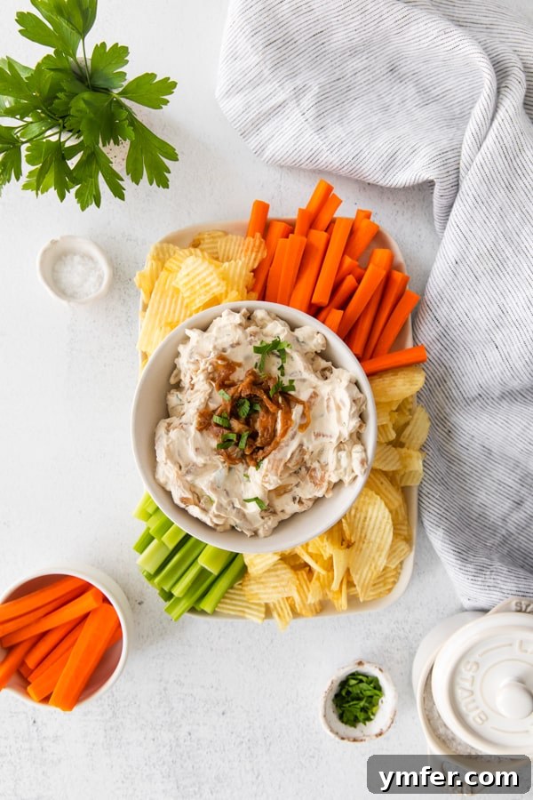 Gourmet Caramelized Onion Dip 5 A festive platter showcasing homemade French Onion Dip surrounded by an abundance of fresh vegetables like carrots and celery, alongside a generous pile of crispy potato chips.