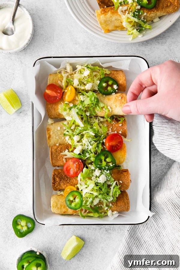 Crispy Air Fryer Chicken Taquitos 6 A hand reaching for a freshly air-fried chicken taquito from a platter.