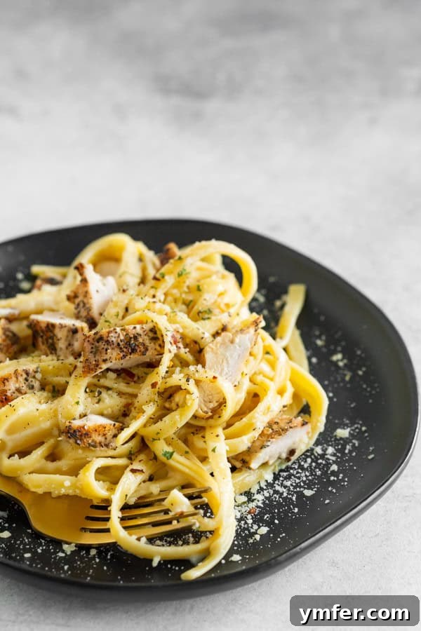 Ultimate Chicken Fettuccine Alfredo 3 Chicken Fettuccine Alfredo on a black plate with a fork.