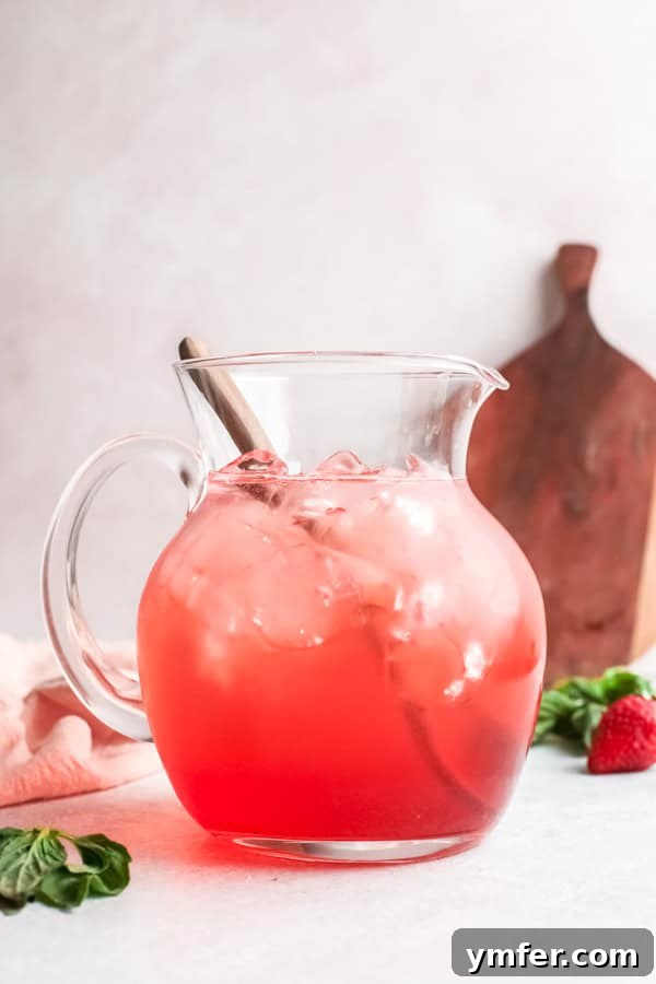 Strawberry Basil Gin Spritzer 3 A pitcher filled with a Strawberry Basil Gin Rickey, ready to be poured, surrounded by fresh strawberries and basil.