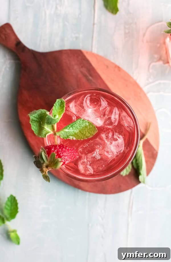 Strawberry Basil Gin Spritzer 4 A close-up of a Strawberry Basil Gin Rickey cocktail, filled with ice and garnished with a strawberry slice and basil leaf.