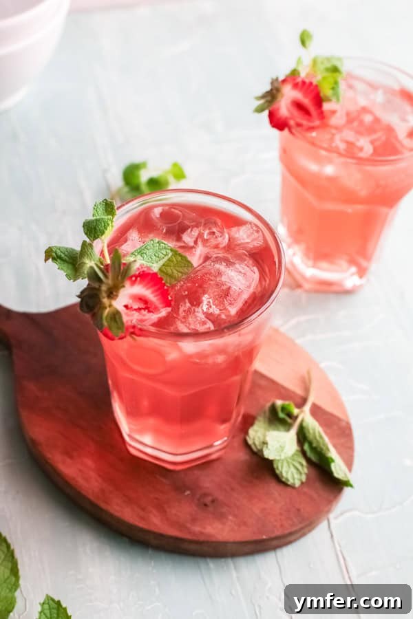 Strawberry Basil Gin Spritzer 5 Two Strawberry Basil Gin Rickey cocktails, garnished with strawberry slices and basil, served on a rustic wooden board.