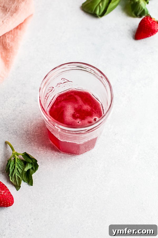 Fresh Strawberry Basil Elixir 6 Process shot: Strawberry basil simple syrup being poured through a fine mesh strainer to remove solids.