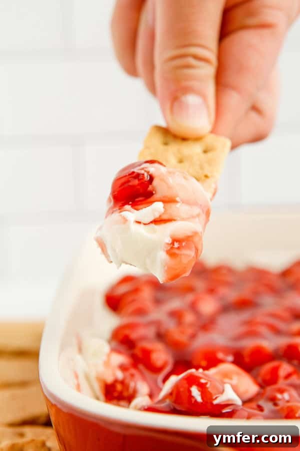 Luscious Cherry Cheesecake Dip 6 A serving spoon scooping a generous portion of Cherry Cheesecake Dip, showcasing its creamy texture and rich cherry topping, ready to be enjoyed with dippers.