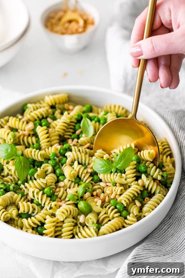 Vibrant Pesto Pasta Salad 6 A serving spoon scooping a generous portion of Pesto Pasta Salad from a large bowl.