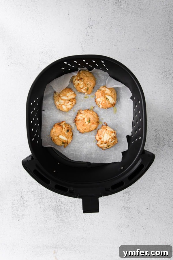 Crispy Air-Fried Crab Cakes 4 Two Air Fryer Crab Cakes cooking inside the basket of an air fryer, turning golden brown.