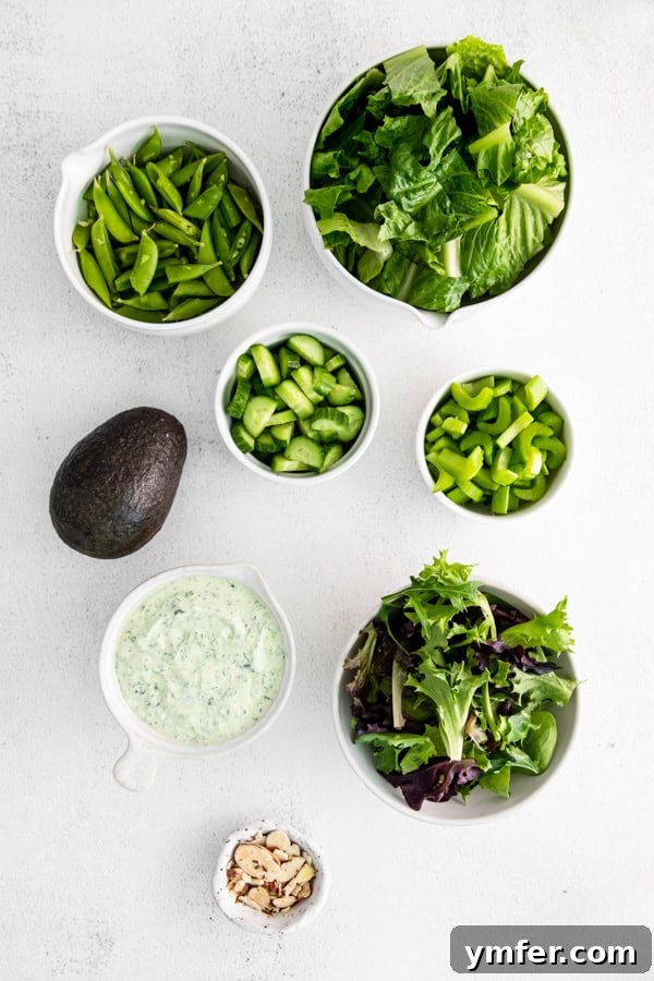 Divine Green Goddess Salad 3 Fresh ingredients laid out for making Green Goddess Salad, including crisp lettuce, cucumbers, snap peas, avocado, herbs, mayonnaise, and sour cream.