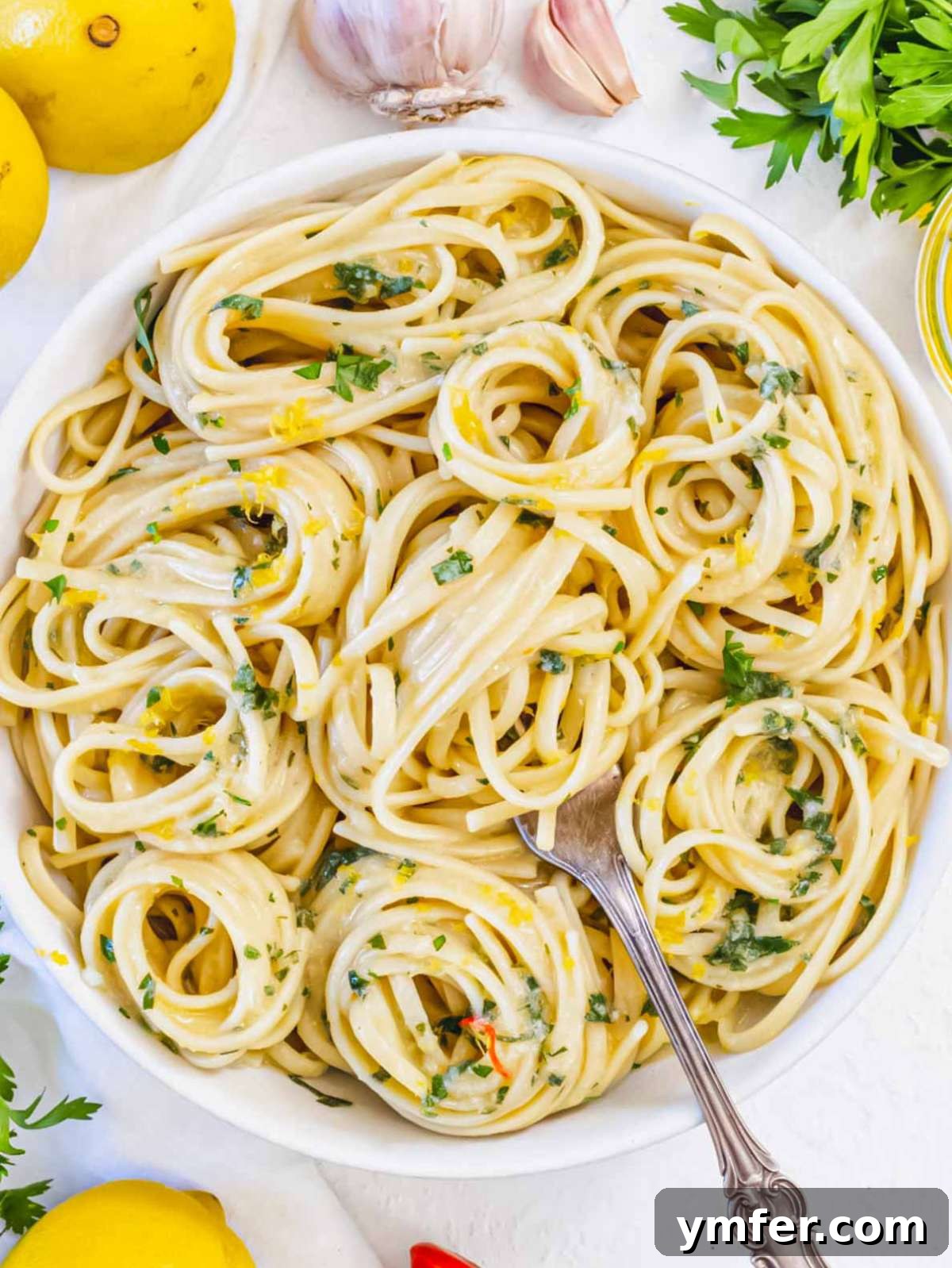 Effortless Lemon Pasta (Creamless) 3 Top-down view of a bowl of lemon pasta without cream, with visible parsley, olive oil, and grated lemon zest top.