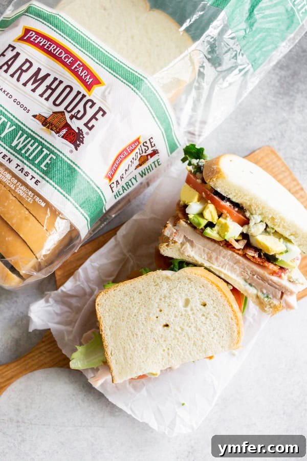 The Ultimate Cobb Sandwich 5 A Cobb Salad Sandwich cut cleanly in half, showcasing its layers of ingredients, on a serving plate.