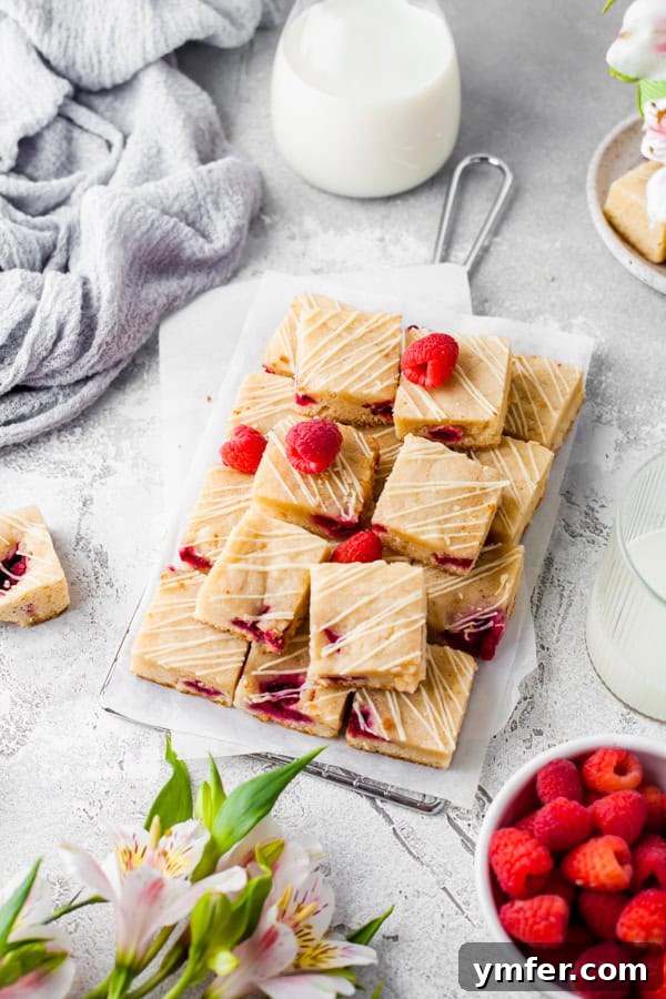 Ruby Raspberry Blondies 2 Stacked white chocolate raspberry blondies on a table, garnished with fresh raspberries.